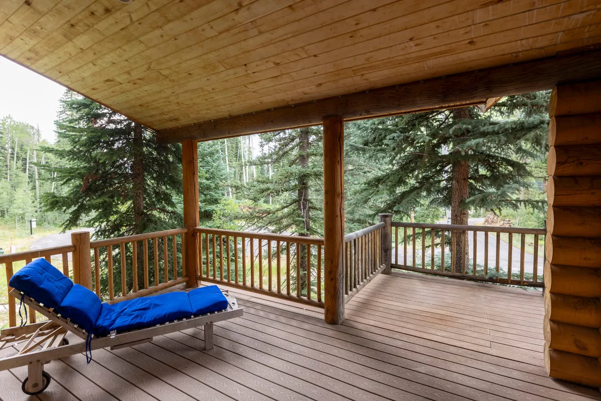This image captures the exterior deck surrounded by trees, featuring a blue lounge chair and peaceful natural surroundings. The scene evokes relaxation and a connection to nature, emphasizing an inviting outdoor area for enjoying meals, morning coffee, or evening toasts with mountain views.