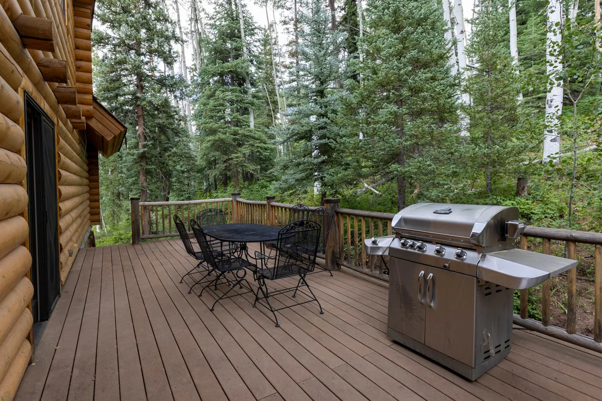 An exterior deck features a grill, a dining table, and surrounding trees, creating an inviting space for outdoor dining. The ambiance is relaxed and nature-centric, suggesting evenings spent barbecuing, enjoying sunset views, or sipping morning coffee amidst the trees.