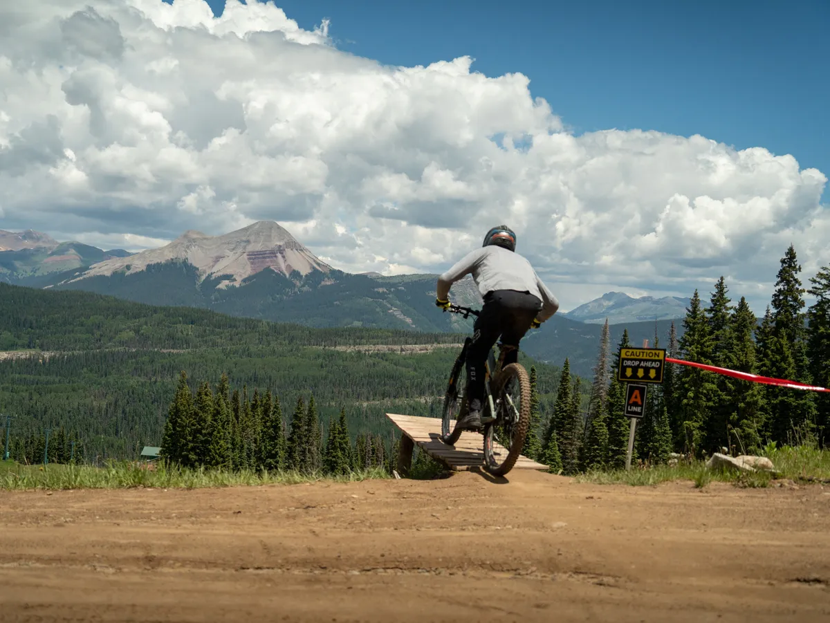 An action-focused exterior image showcasing a mountain biker mid-ride on a trail, with a dramatic mountain backdrop and lush forest surroundings. The scene exudes energy, adventure, and the thrill of outdoor sports, reinforcing the area's appeal to adventure seekers.