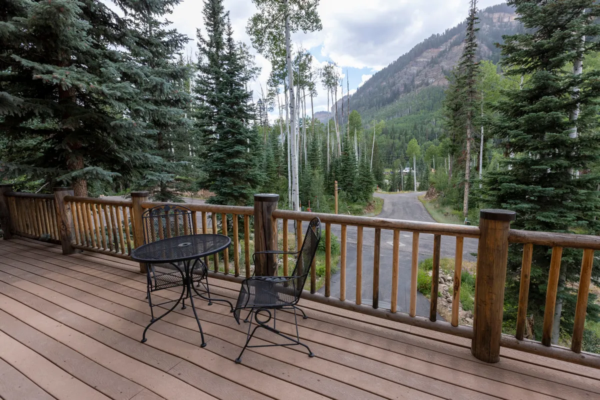 A peaceful outdoor setting with a table and chair nestled among trees, looking out at distant mountains. The atmosphere is serene, ideal for enjoying coffee, reading a book, or simply soaking in the natural surroundings throughout spring and summer.