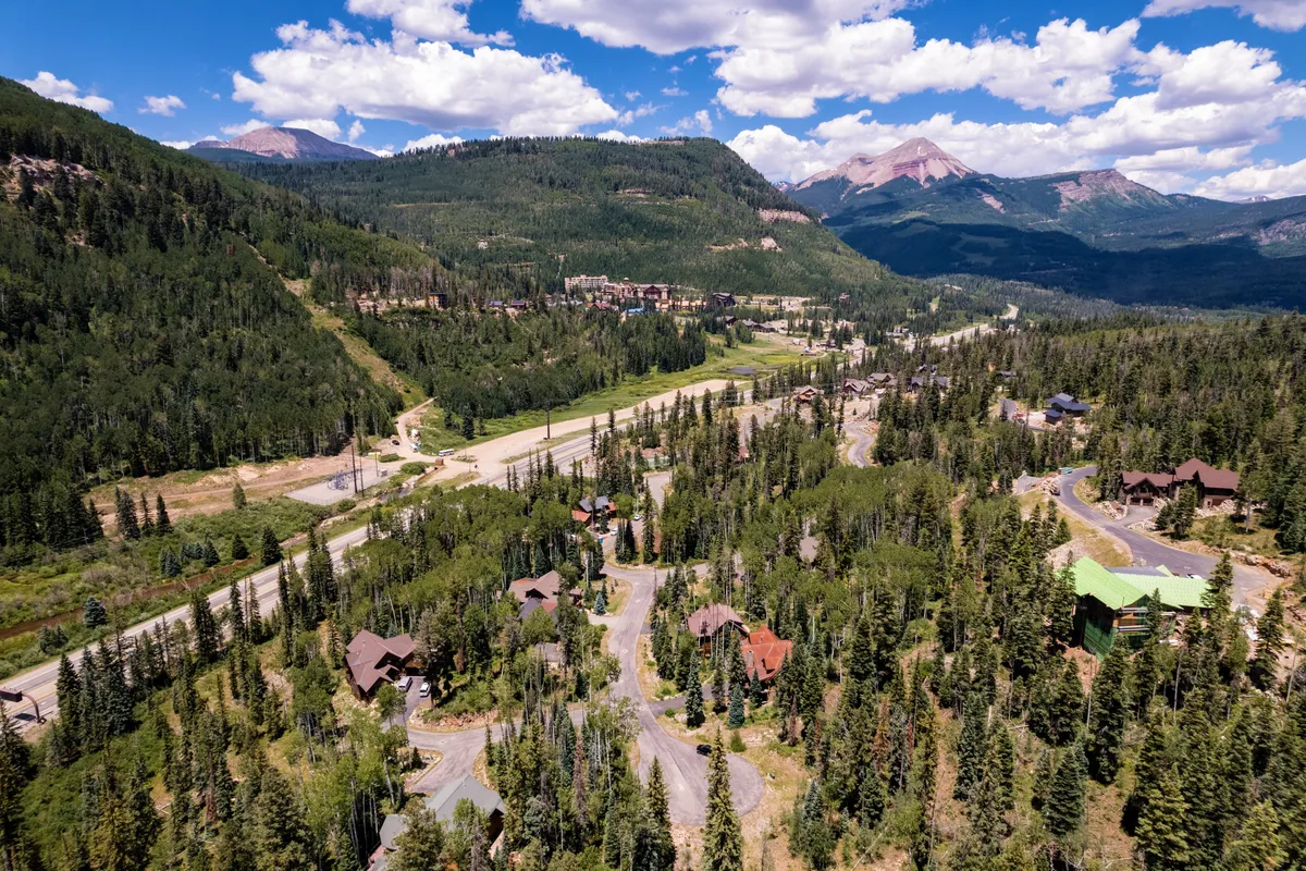A panoramic exterior shot revealing a vast mountain range, dense forest, scenic roads, and homes tucked among the trees. The image conveys a sense of scale and possibility for all kinds of outdoor adventure, from hiking and biking to wildlife watching and stargazing.