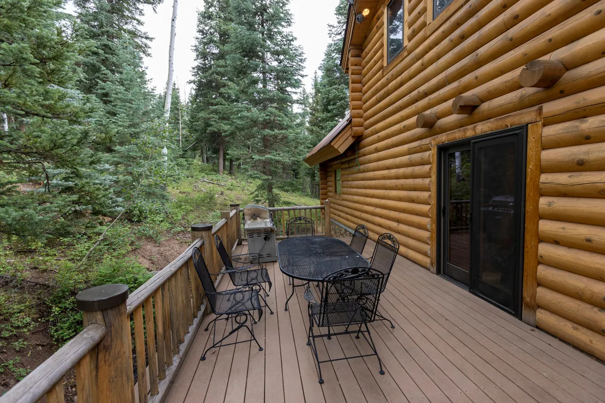 This exterior shot presents the log cabin’s façade, a dining table on the deck, and surrounding trees, evoking peacefulness and a strong connection to nature. The setup is perfect for outdoor dining and gatherings, highlighting family-friendly activities.