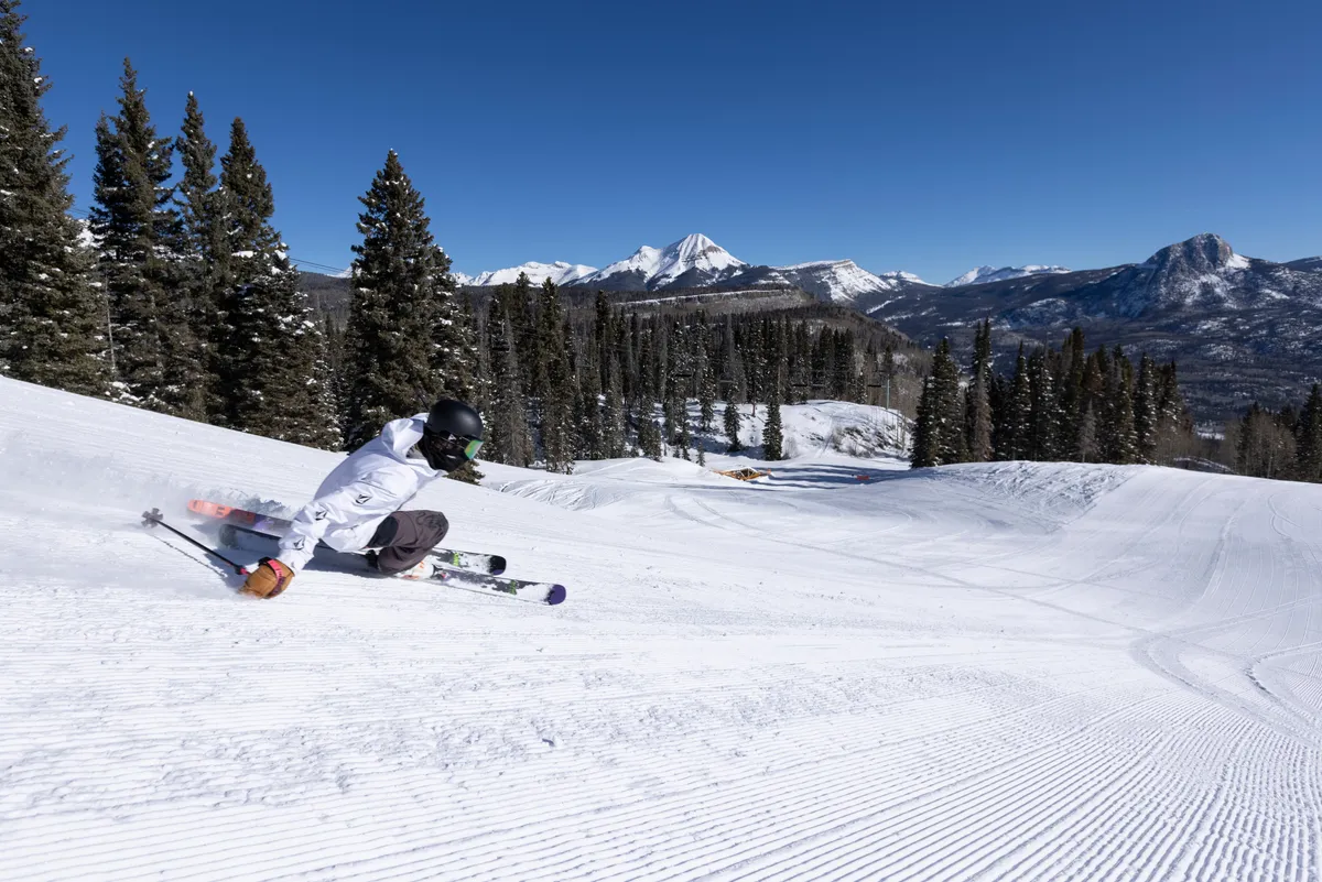 A skier is captured in mid-motion gliding down snow-covered slopes, with distant mountains providing a breathtaking backdrop. The landscape is blanketed in fresh snow, encapsulating the excitement of winter activities in a natural alpine setting.