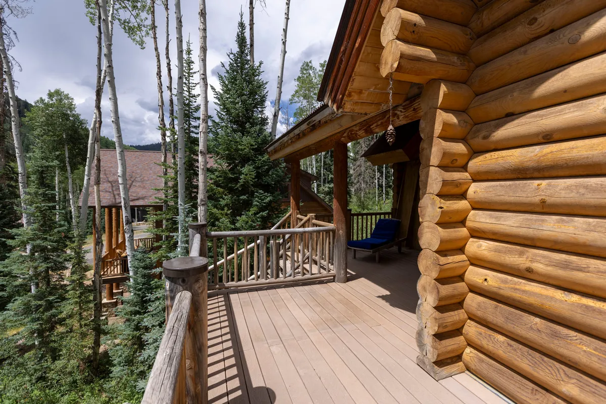 This image shows a wooden deck attached to a log cabin, with a cozy deck chair nestled among the trees. The deck overlooks peaceful forest scenery, inviting guests to unwind outdoors and take in the views.