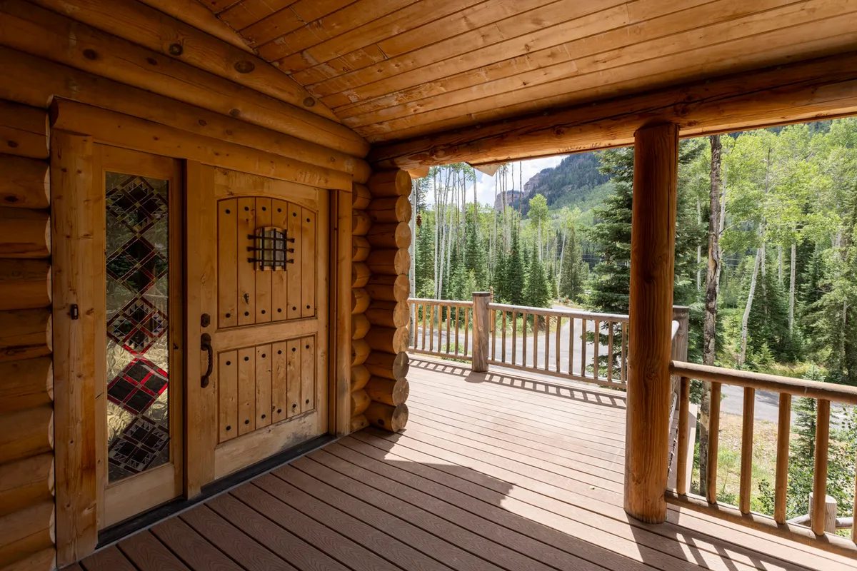 This image offers a view from inside looking out toward the deck, with log walls and a wooden door opening to natural scenery. It highlights the seamless transition between indoor coziness and the outdoor environment, suggesting an inviting space to relax, socialize, and take in the views.