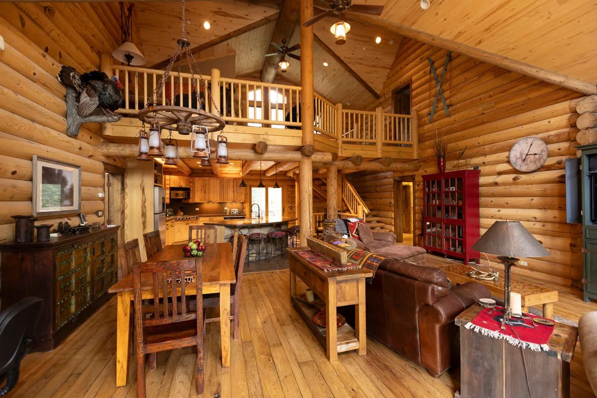 This photo offers a broad perspective of the open-plan living, dining, and kitchen areas, featuring wooden beams, a prominent dining table, a comfortable sofa area, and visible kitchen counters. The layout encourages both relaxation and group activities, with a homey, cohesive atmosphere.